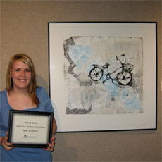Student stands next to her framed artwork with an award.